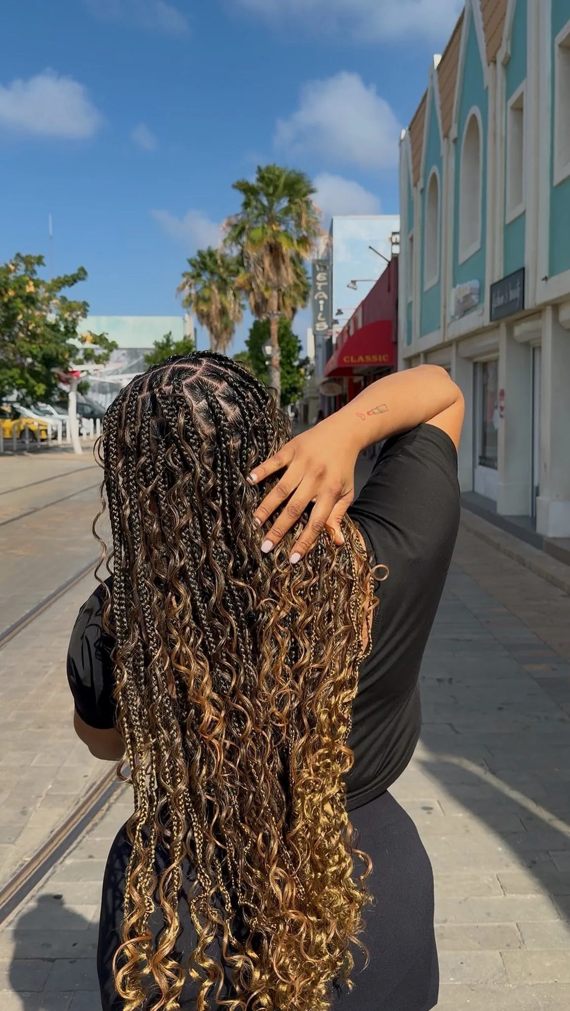 Client showcasing long golden boho goddess braids with loose curls on Caya Betico Croes street in Aruba